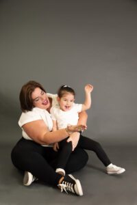 Una madre sostiene con ternura a su pequeña hija mientras comparten una risa espontánea, reflejando el amor incondicional en el Día de la Madre.